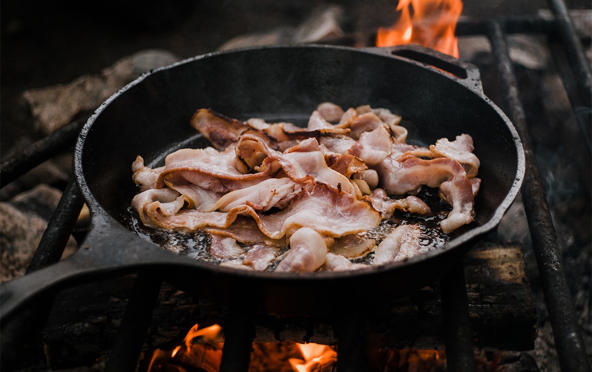 a pan of sizzling bacon over coals